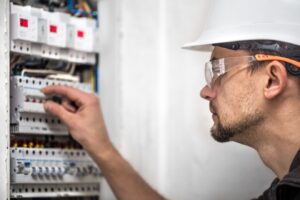Electrical technician working on a switchboard with fuses, installing and connecting electrical equipment.